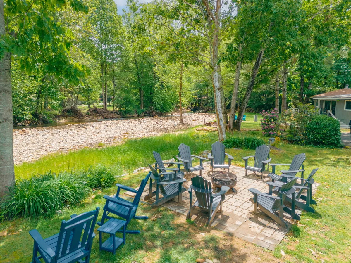 A riverside fire pit with Adirondack chairs, overlooking the gentle flow of the river and framed by lush greenery. The setting invites campfire gatherings, riverside relaxation, and connection with nature.