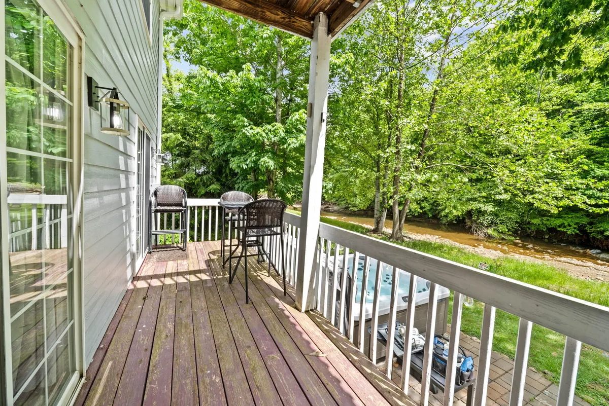 A tranquil wooden deck set amid lush greenery, overlooking a nearby water stream. Comfortable outdoor seating invites guests to relax, enjoy nature, and listen to the sounds of the stream in a peaceful setting.