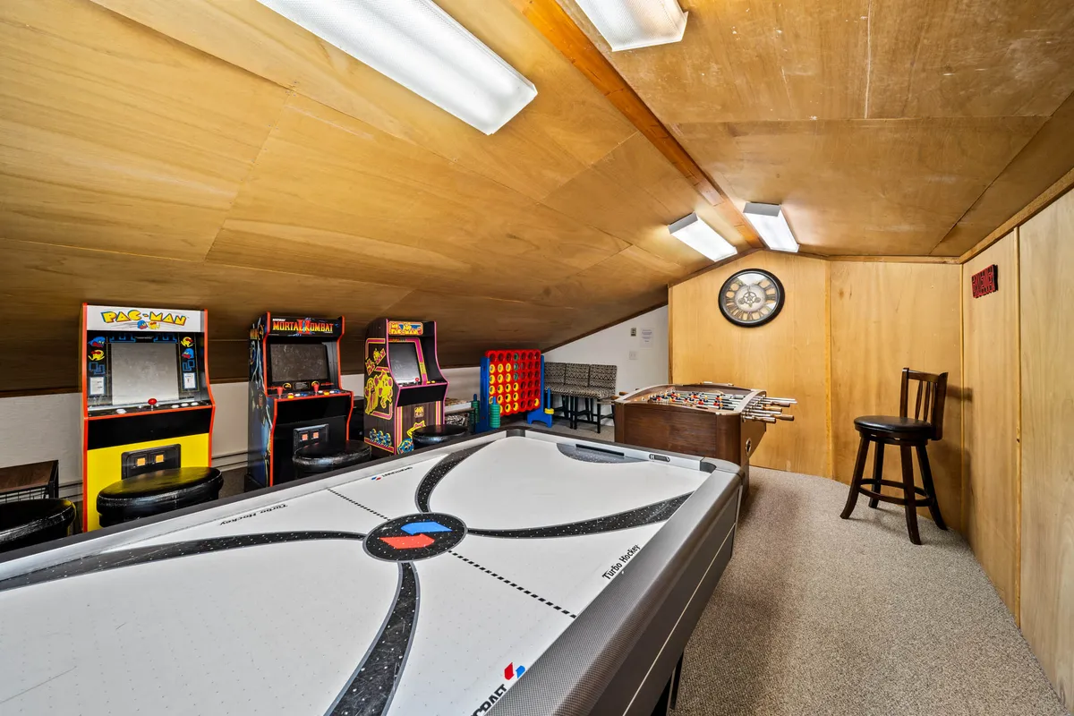 A dynamic interior with an air hockey table, a row of arcade game machines, a foosball table, and a wooden chair. The room is brightly lit and designed for active play, creating an inviting atmosphere for kids and nostalgic adults alike.