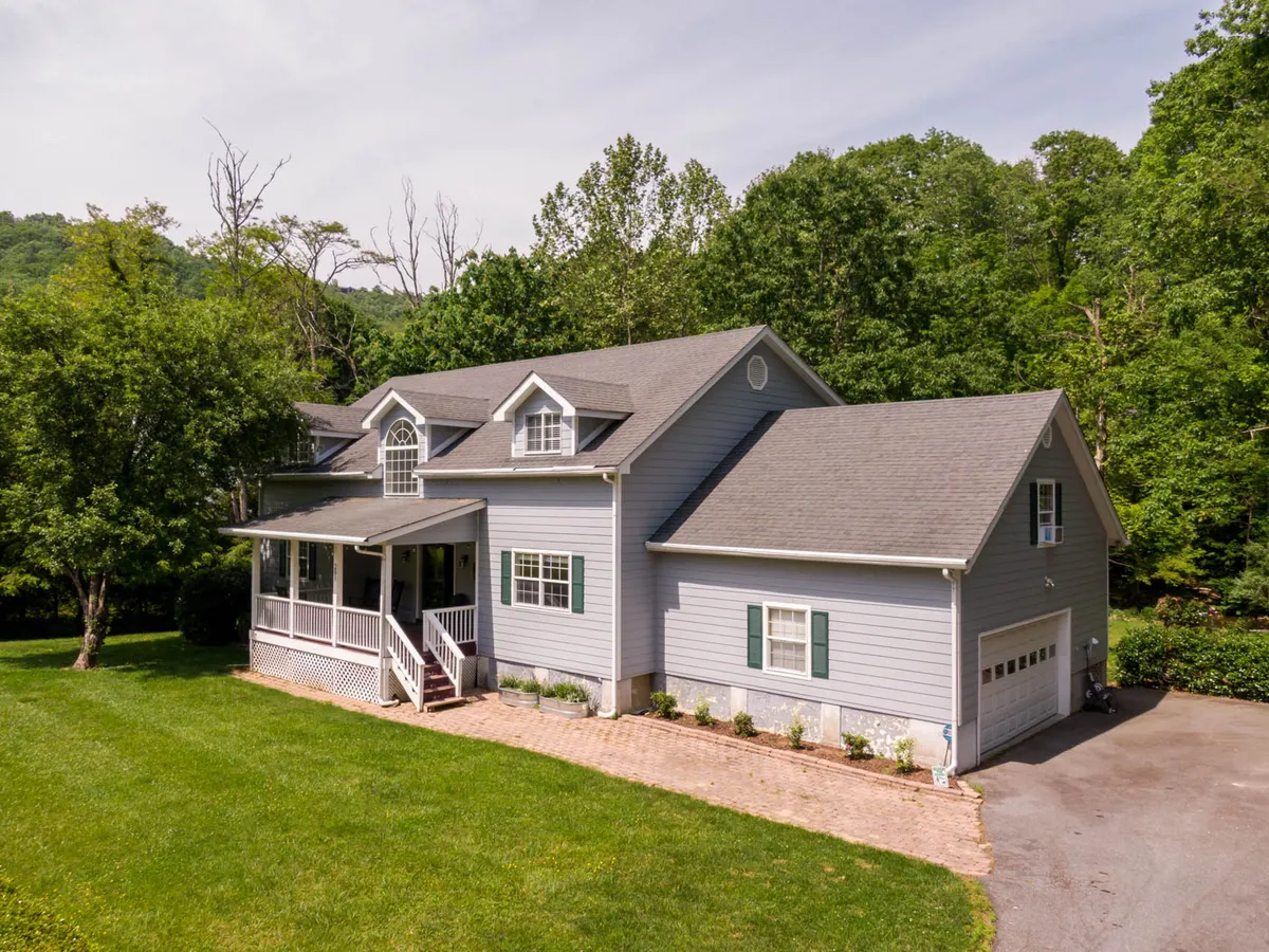 A wide exterior view of the Riverwood house, featuring the welcoming front porch, lush lawn, and mature landscaping. The spacious yard stretches out in front, surrounded by greenery, making it ideal for outdoor recreation, relaxation, or playtime with pets.