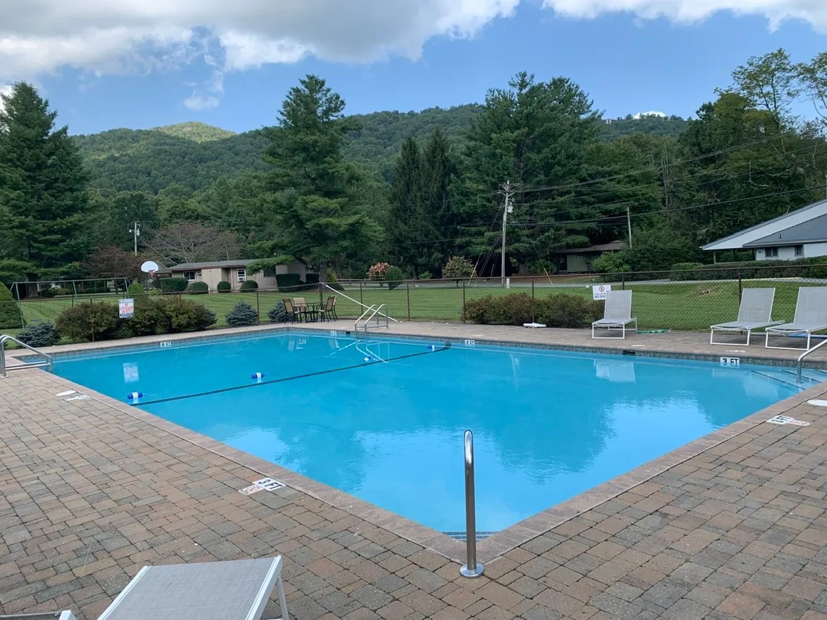 A scenic view of the swimming pool surrounded by greenery, mountains in the distance, and poolside lounge chairs. The setting speaks to both activity and relaxation, perfect for socializing and enjoying resort-style amenities just steps from the home.