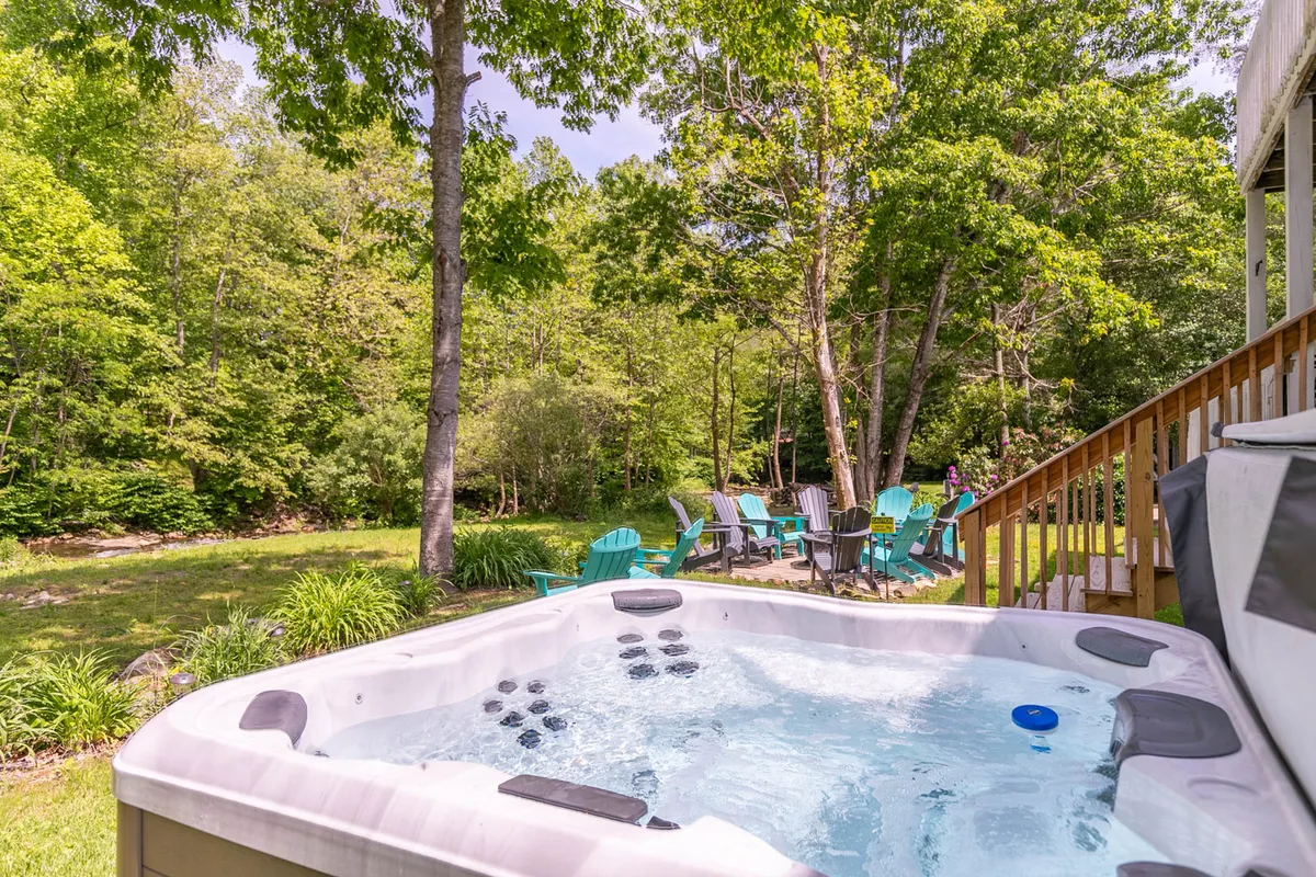 An inviting outdoor area featuring a private hot tub surrounded by Adirondack chairs, set amid lush greenery. The relaxed atmosphere is highlighted by the suggestion of stargazing or unwinding after a day of adventure.