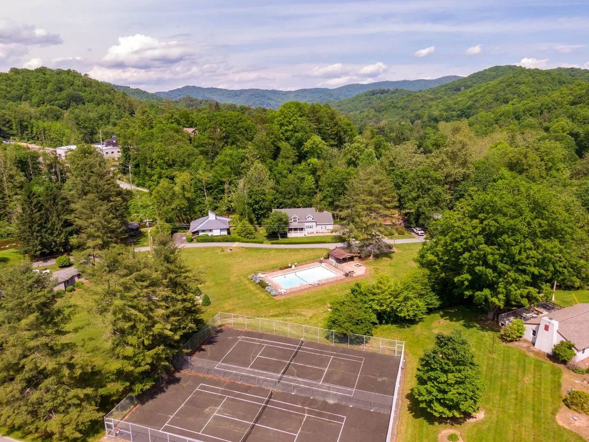 A bright exterior scene showing a swimming pool, tennis courts, and surrounding mountains, with the main house in the background. The area is vibrant and ideal for recreation or relaxation.