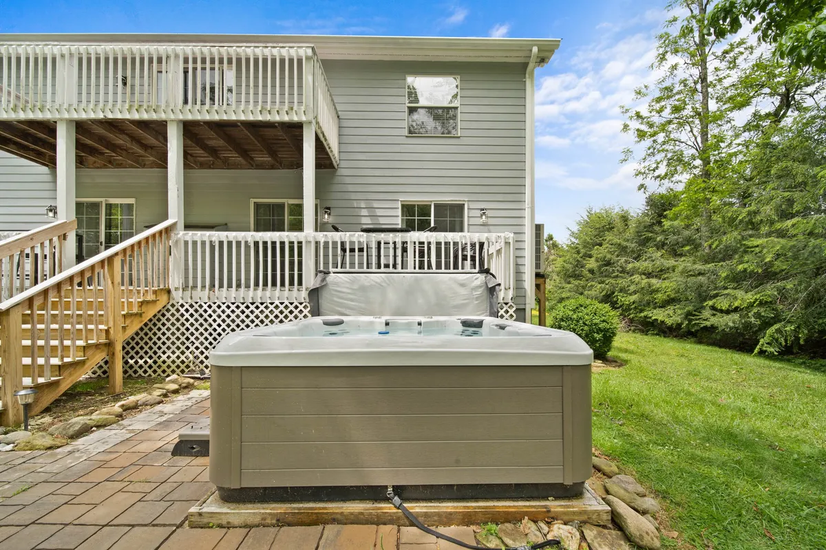 This image shows a renovated back deck with a hot tub surrounded by lush greenery, offering a tranquil space for relaxation. The deck has ample space for entertaining guests and enjoying nature views.