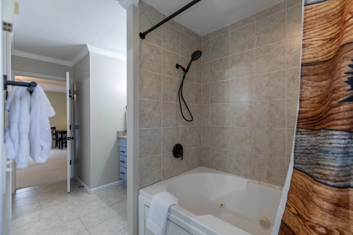A tranquil bathroom scene showing a jetted jacuzzi tub with a shower head, textured shower curtain, and soothing color tones. The space feels luxurious and inviting, ideal for a restorative bath or shower.